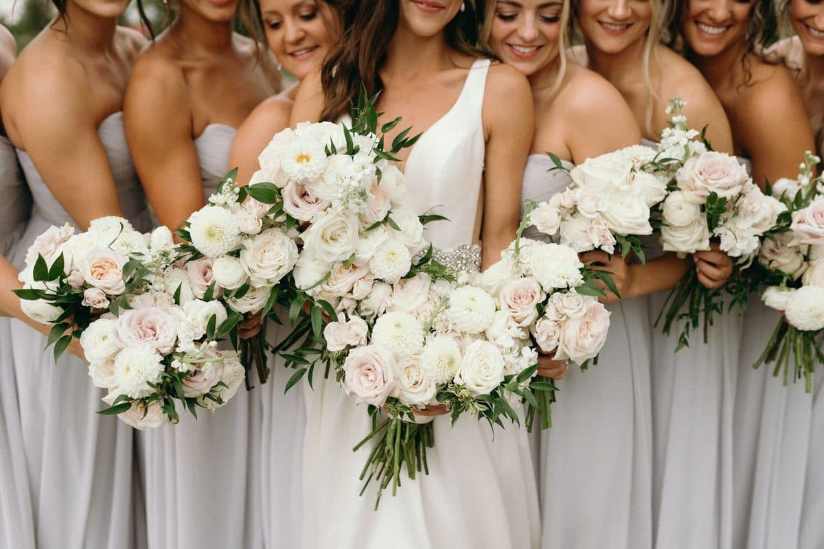 Bride and bridesmaids in a row, each holding a white and blush bouquet