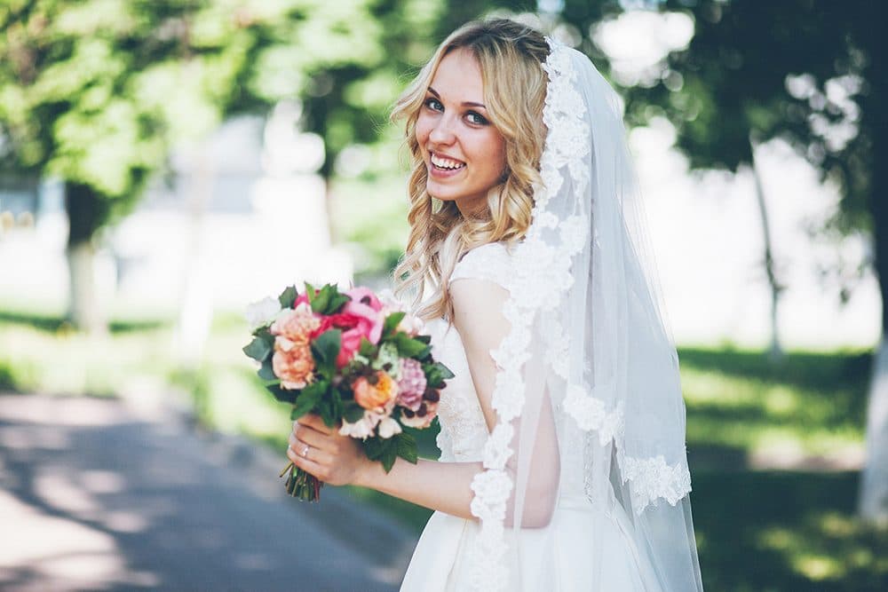 Smiling bride in a lace veil holding a pink bouquet