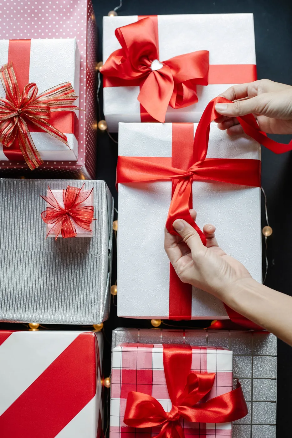 Hands carefully tying a red ribbon around a Christmas gift